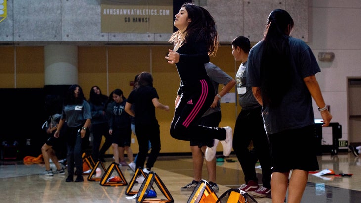 Teenage girl jumping during high school gym class.