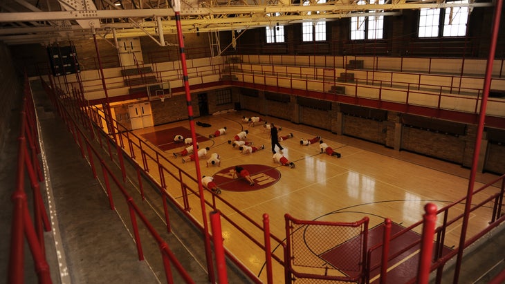 A teacher observes students performing pushups in a high school gym.