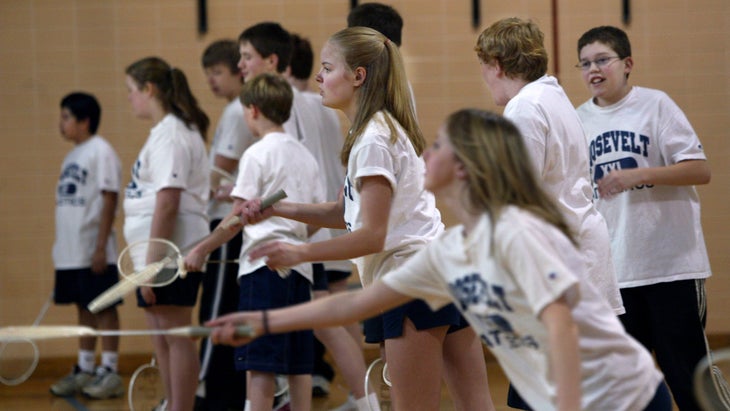 Middle school students holding badminton rackets in a gym