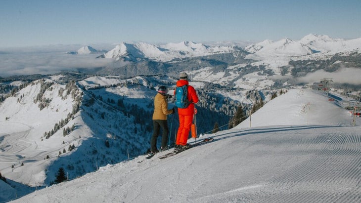 A couple in ski wear pause on snowy slopes overlooking the resort village of Morzine, France.