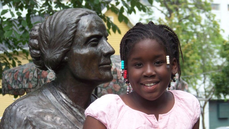 A little girl sits next to the statue of famous Rochester, New York, suffragette Susan B. Anthony.