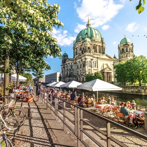 Cafe tables with umbrellas are set up alongside Berlin’s Spree Riverfront.