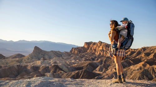 Young mom hiking with toddler in backpack, standing on rocky plateau