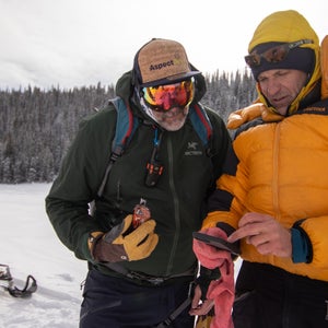 Two skiers look at their phone in the backcountry with a snowmobile in the background