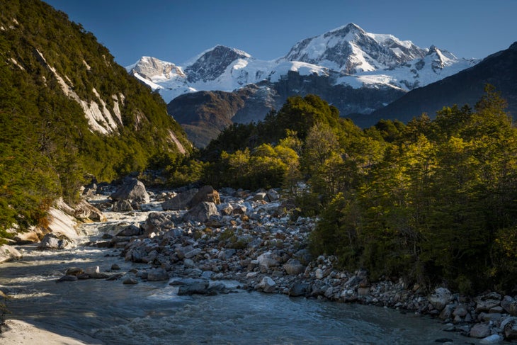 A wide, rock-filled river descends from snowcapped peaks in Chile's Aysén region.