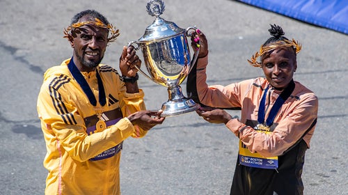 Two Boston Marathon winners hold up a victory trophy.