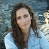 Writer Heather Hansman sits near a river, looking into the camera and wearing a denim shirt