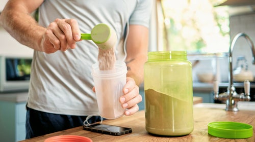 Closeup of one man pouring a scoop of chocolate whey protein powder