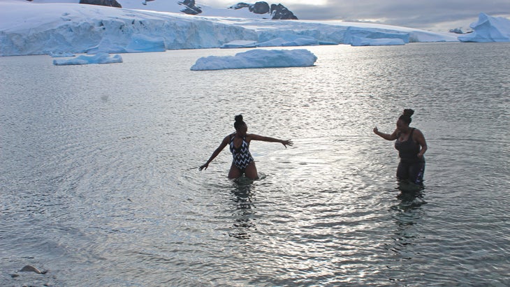 two women with HX (Hurtigruten Expeditions) on an iceberg-lined beach in Antarctica