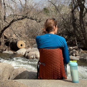 woman sitting on Crazy Creek chair beside stream