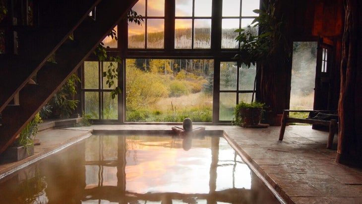 A woman soaks in Dunton's bathhouse, whose large windows look out at the mountains and a grove of aspens.