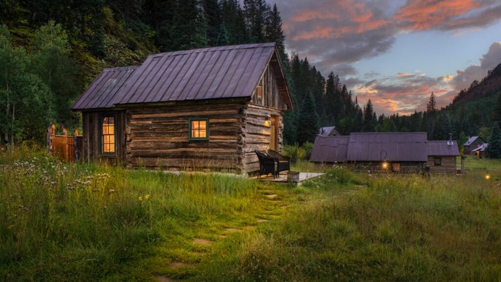 The cabin Echo set against the hillside and wild grasses of summer, with a pathway leading to its entrance and two chairs.