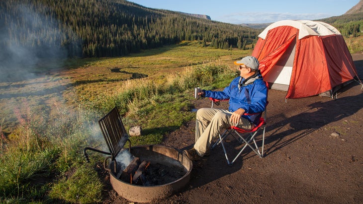 Man sitting by campfire at campsite in Flat Tops Wilderness area, northwest Colorado.