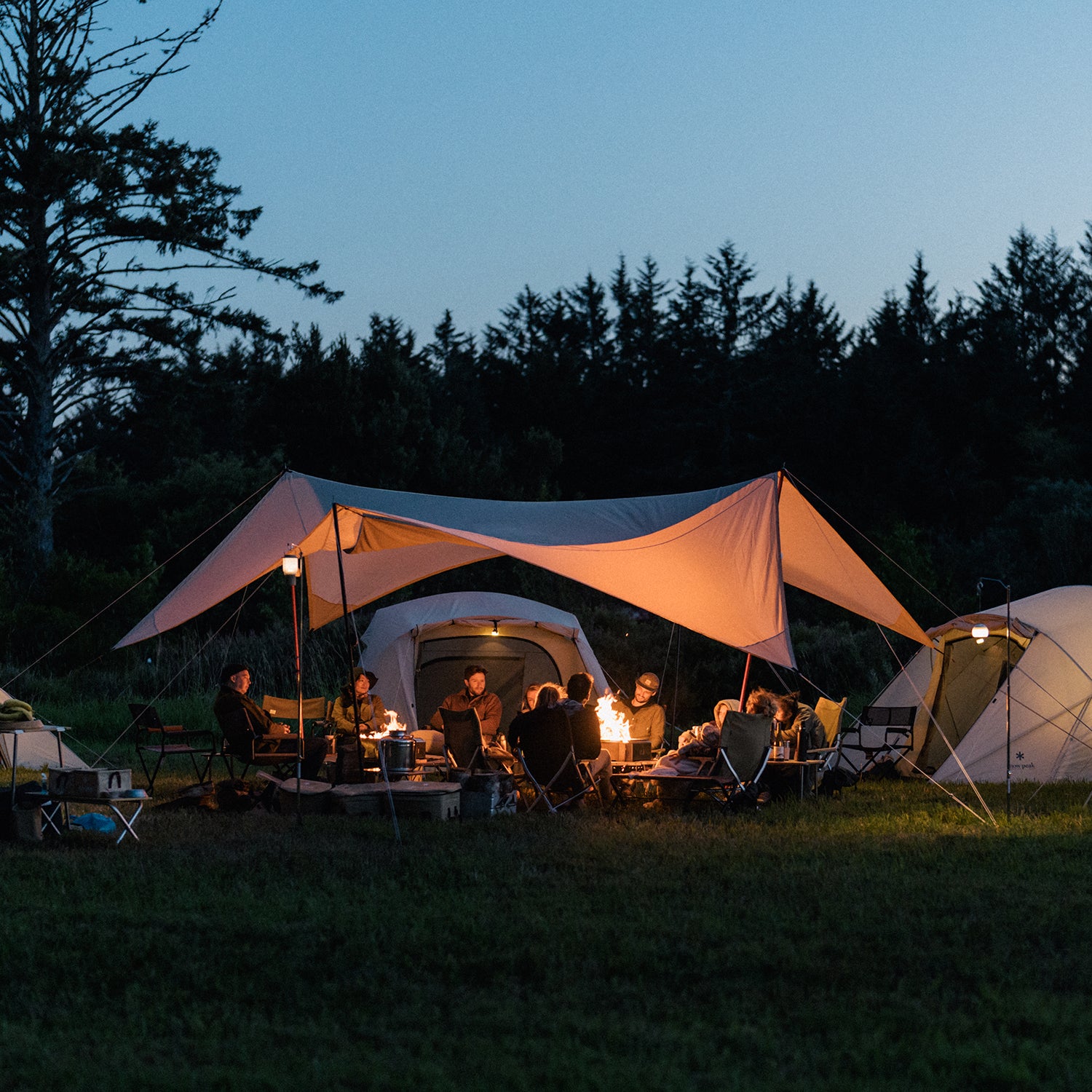 People lounging around a campfire surrounded by Snow Peak camping gear