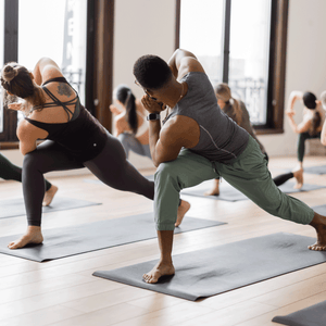 Class of yoga students being instructed by a teacher through a vinyasa yoga sequence