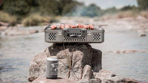 Nomad grill and smoker with steam rising on top of rock in front of lake