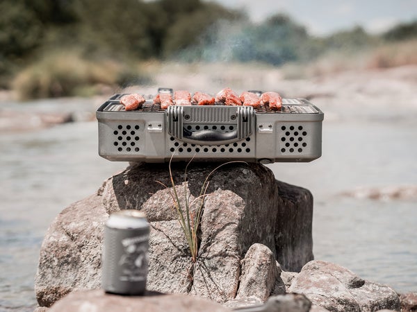 Nomad grill and smoker with steam rising on top of rock in front of lake