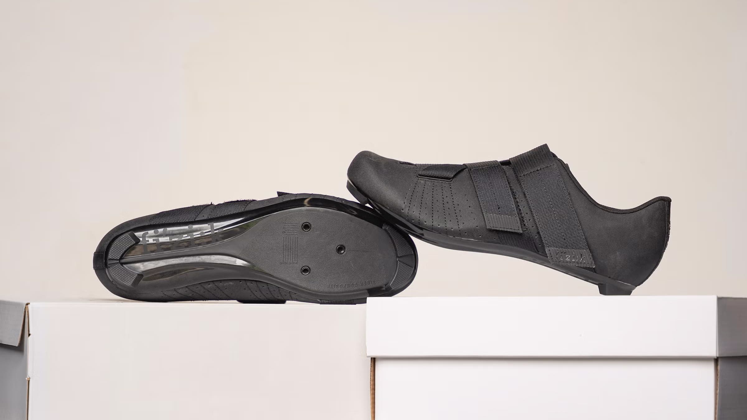 Black cycling shoes displayed on shoeboxes on off-white background