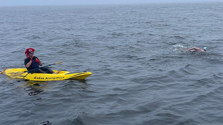 A kayaker paddles a yellow kayak next to a swimmer. 