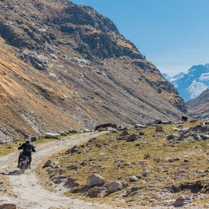 Man riding a motorcycle on a gravel trail through mountains in India