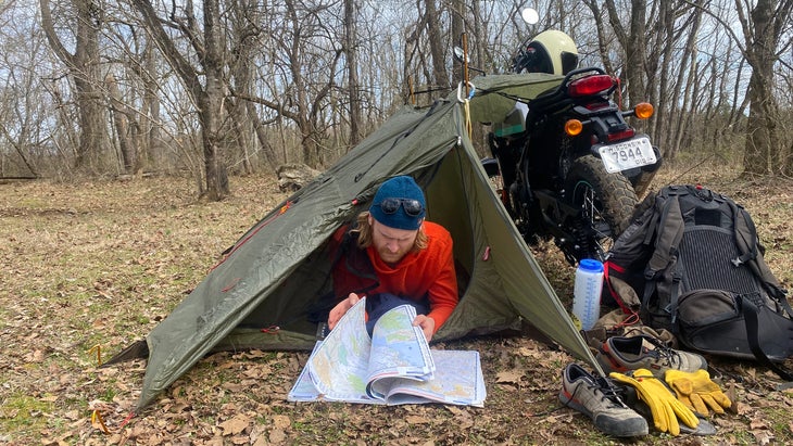 Closeup of man lying in one-man shelter reading road maps