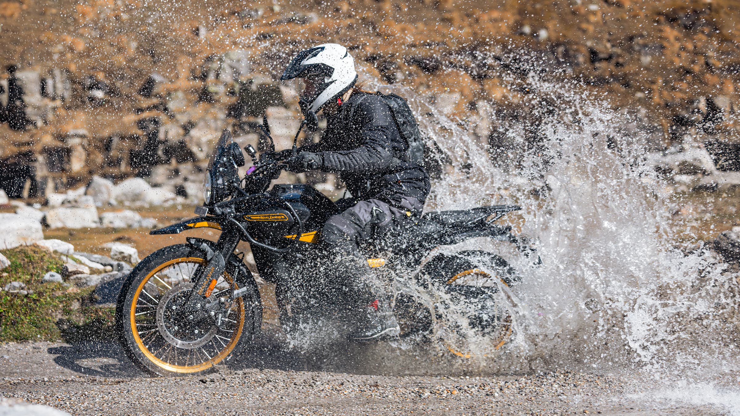 Man riding motorcycle through water on gravel trail