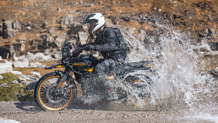 Man riding motorcycle through water on gravel trail 