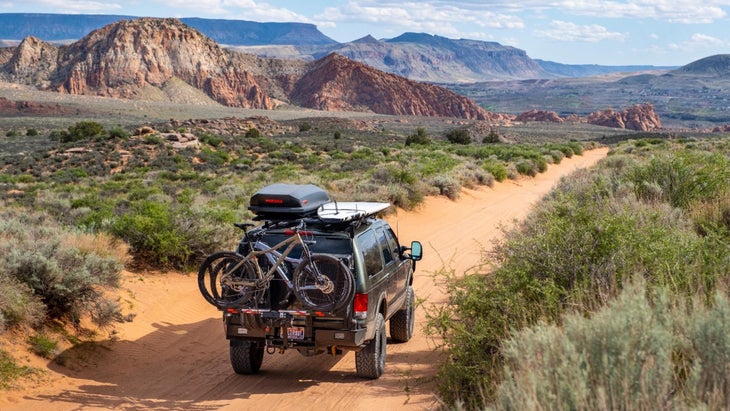 Ford Excursion pickup truck loaded with bikes and gear driving on dirt road in desert 