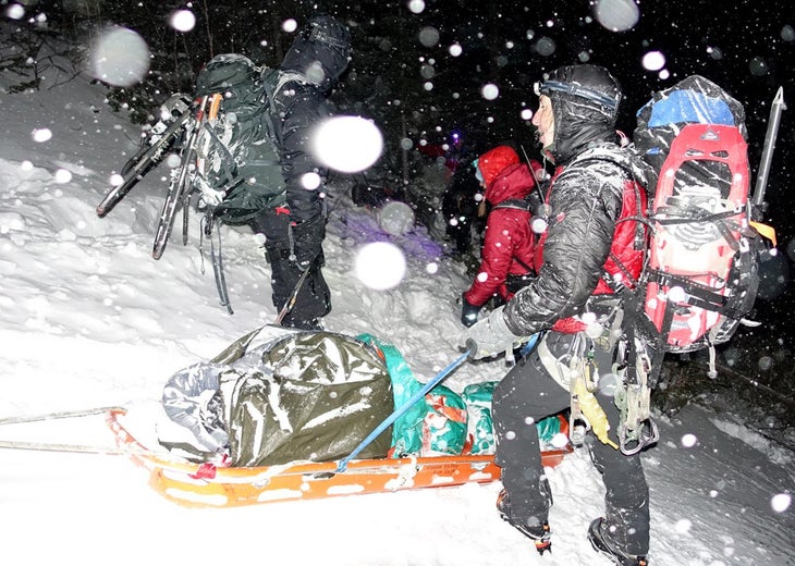 Three rescuers in outdoor gear stand around a patient on a sled in a blizzard during an evacuation