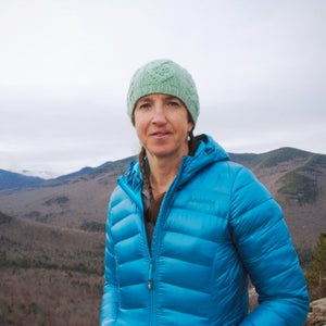 Robbi Mecus looks at the camera with mountains in the background. She is wearing a turquoise beanie and a blue puffy jacket.