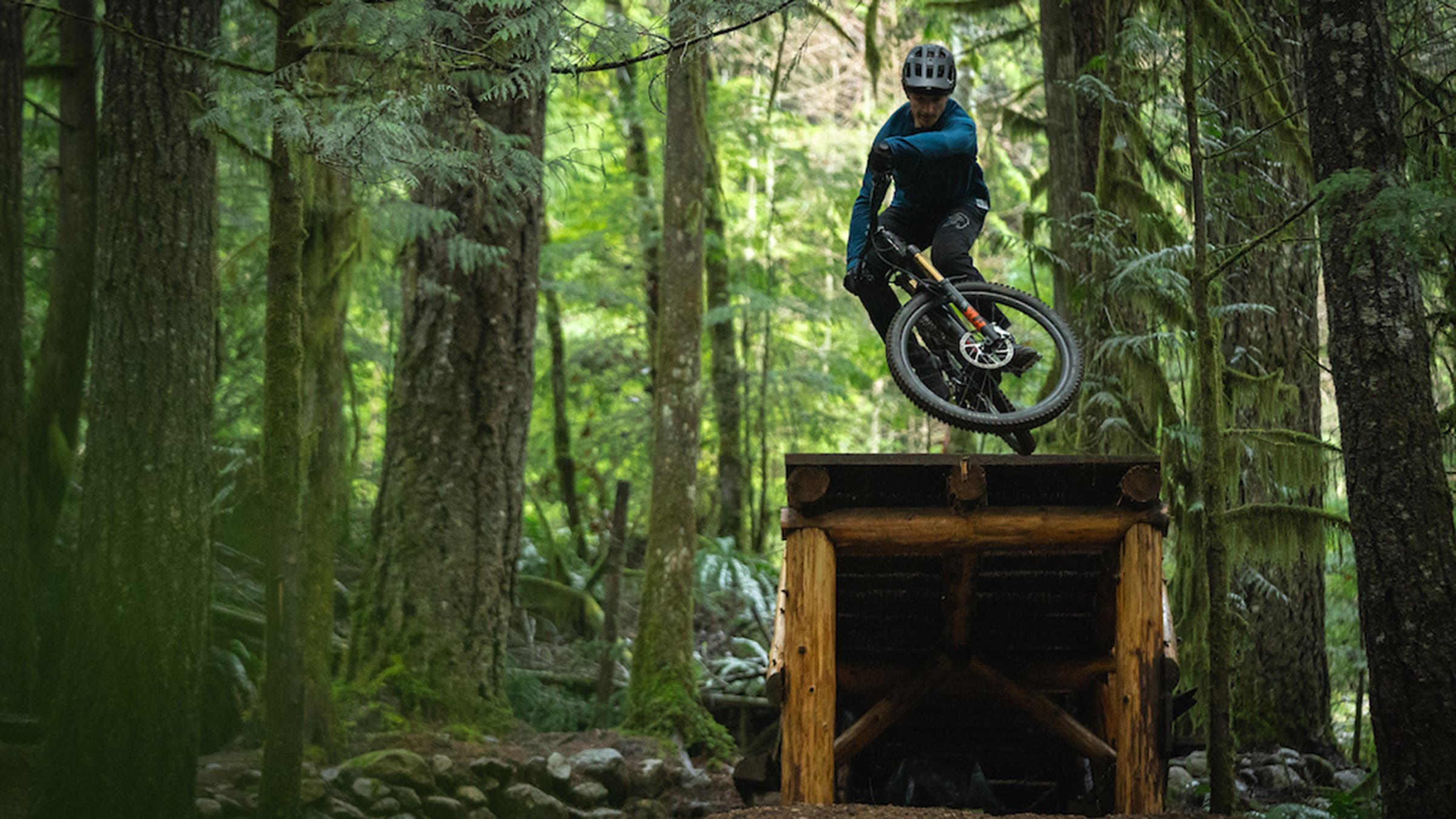 Mountain biker jumping off wooden ramp in woods on electric mountain bike