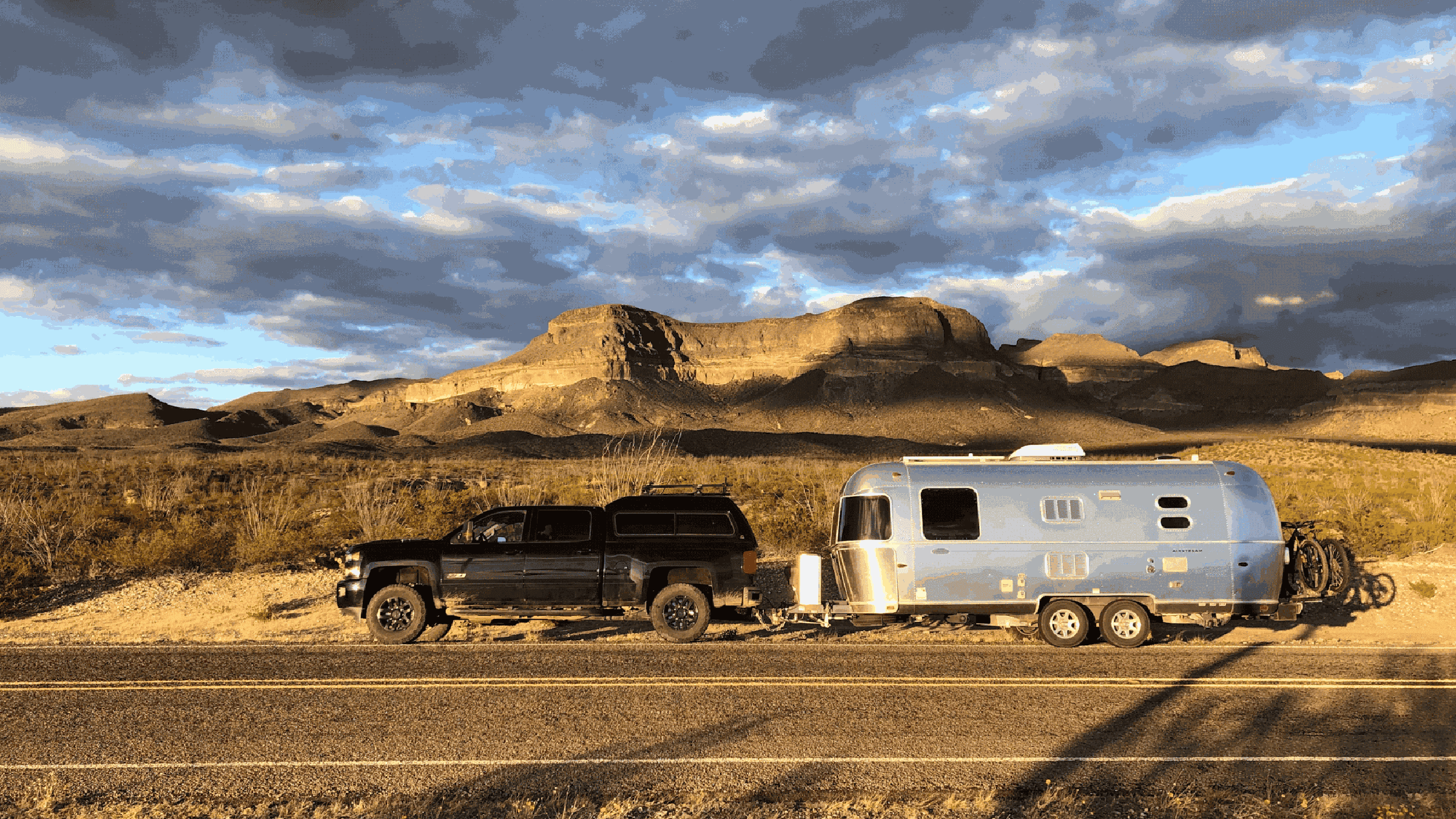 Pickup truck towing an Airstream trailer parked on side of road in desert.