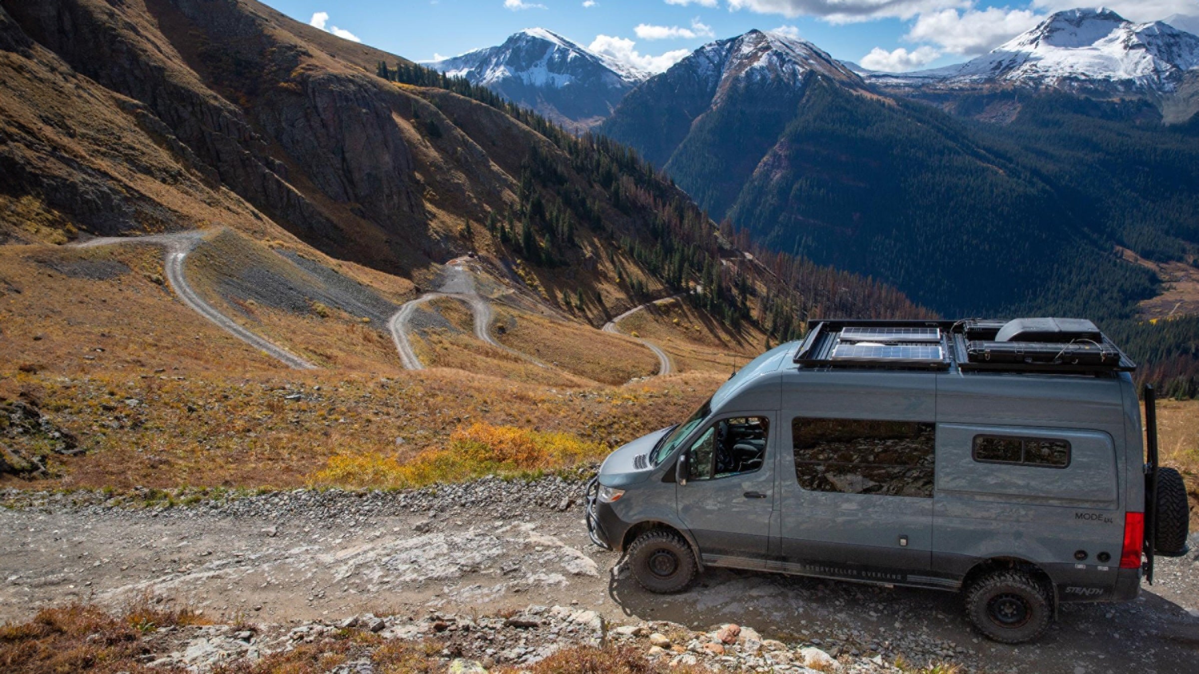 Grey 4x4 van on non-paved mountain pass with mountain peaks in the background