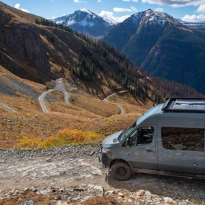 Grey 4x4 van on non-paved mountain pass with mountain peaks in the background