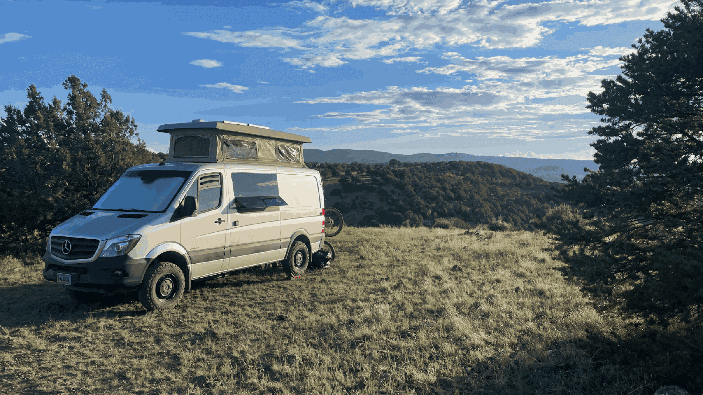 Sprinter van with pop up camper parked on grassy orverlook