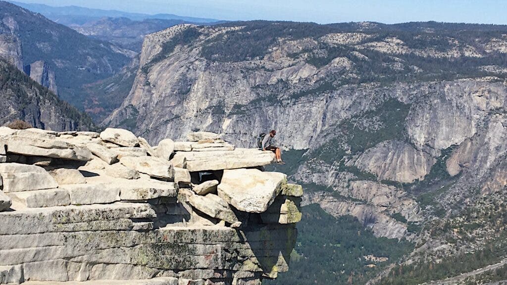 A hiker sits on a precipice atop Yosemite’s Half Dome, with incredible views over the Sierra.