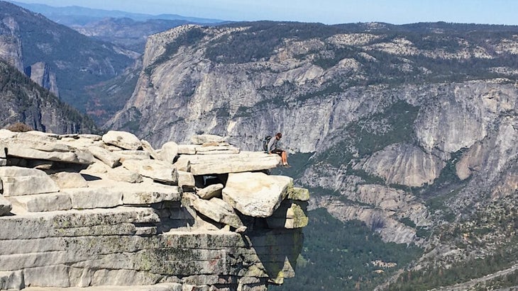 A hiker sits on a precipice atop Yosemite’s Half Dome, with incredible views over the Sierra. 