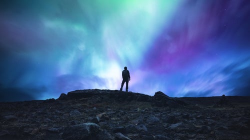 Man standing in the middle of an Icelandic wilderness and watching aurora borealis.