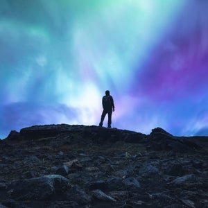 Man standing in the middle of an Icelandic wilderness and watching aurora borealis.