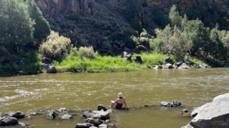 A woman sits on stones at Black Rock Hot Springs along New Mexico's Rio Grande