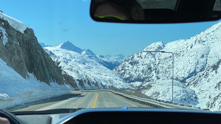 The view from a driver's window. The highway is surrounded by snowy mountains.