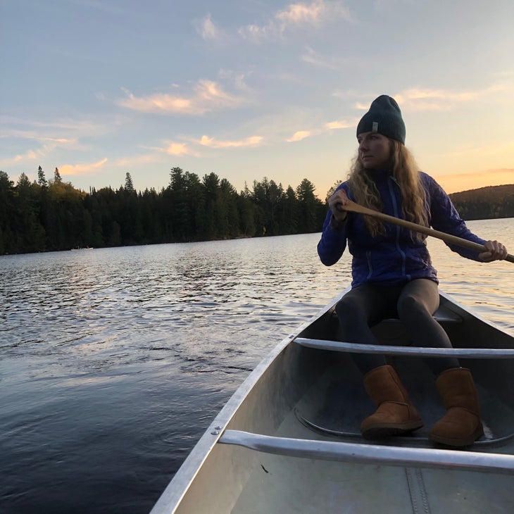 a woman paddling a canoe at sunset