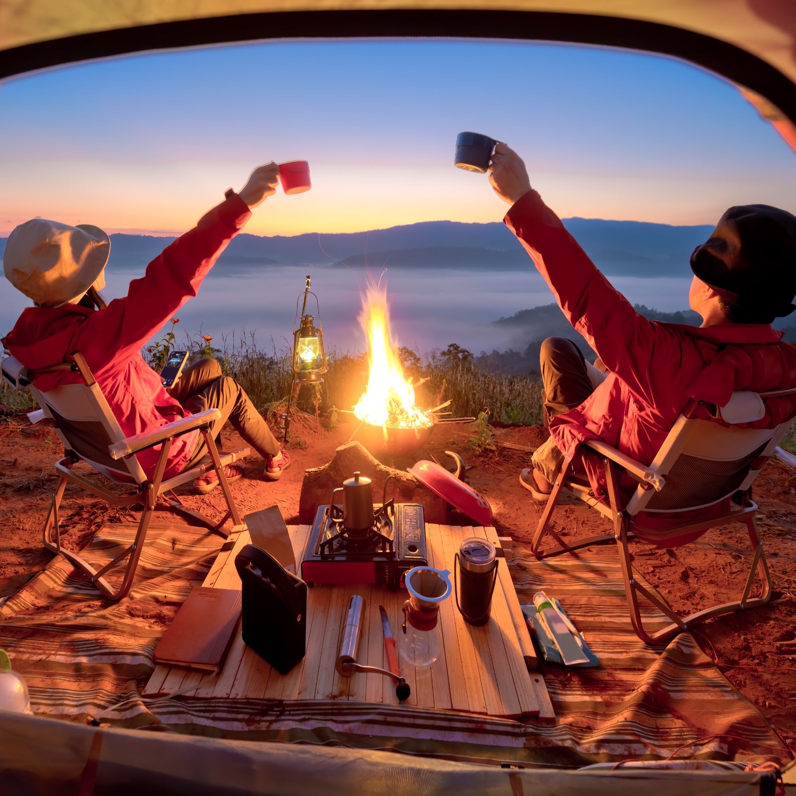 A couple toasts right outside of their tent in front of a campfire.