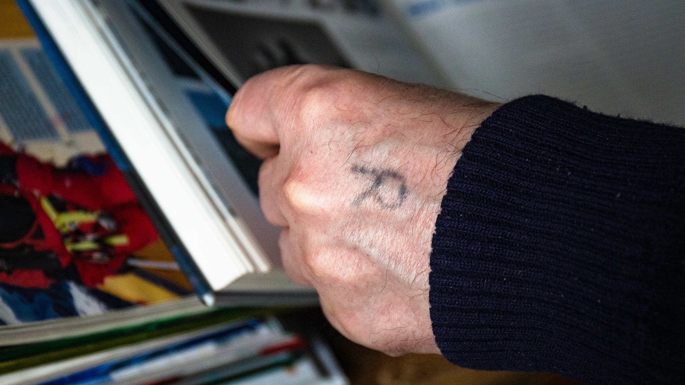 A close-up photo of a man's hand with an "R" tattooed on the back of it