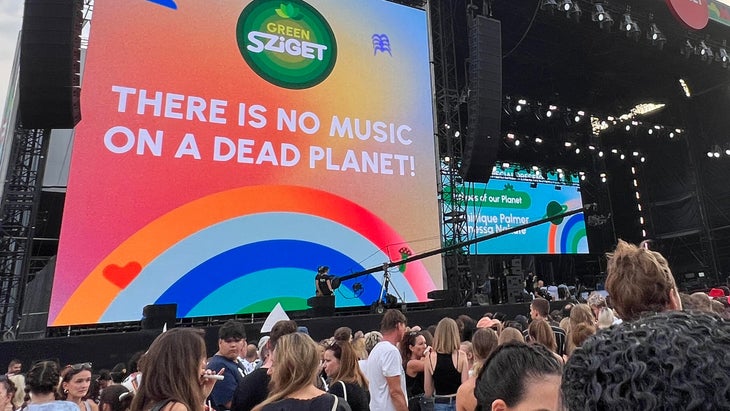 Festival stage and crowd with "There is no music on a dead planet" on big screen