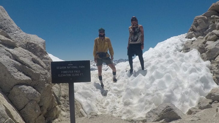 The author and a hiking pal stand atop a snow-covered Forester Pass in Sequoia National Park, next to a sign reading "Elevation 13,200 feet."