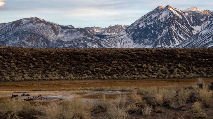 A group of people soak in a thermal pool in a field with beautiful views of Mammoth Mountain, California.