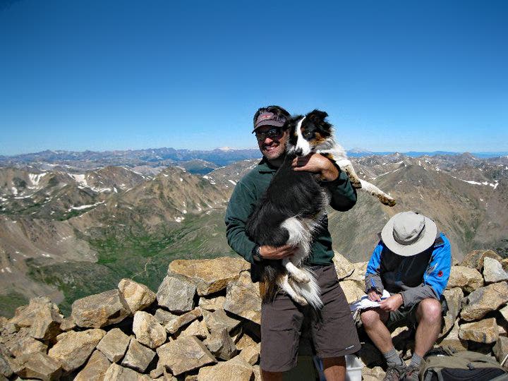Man holding a dog on the top of a high mountain