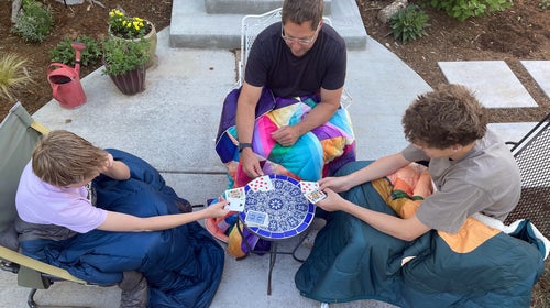 three men playing cards outside with camp blankets around their legs