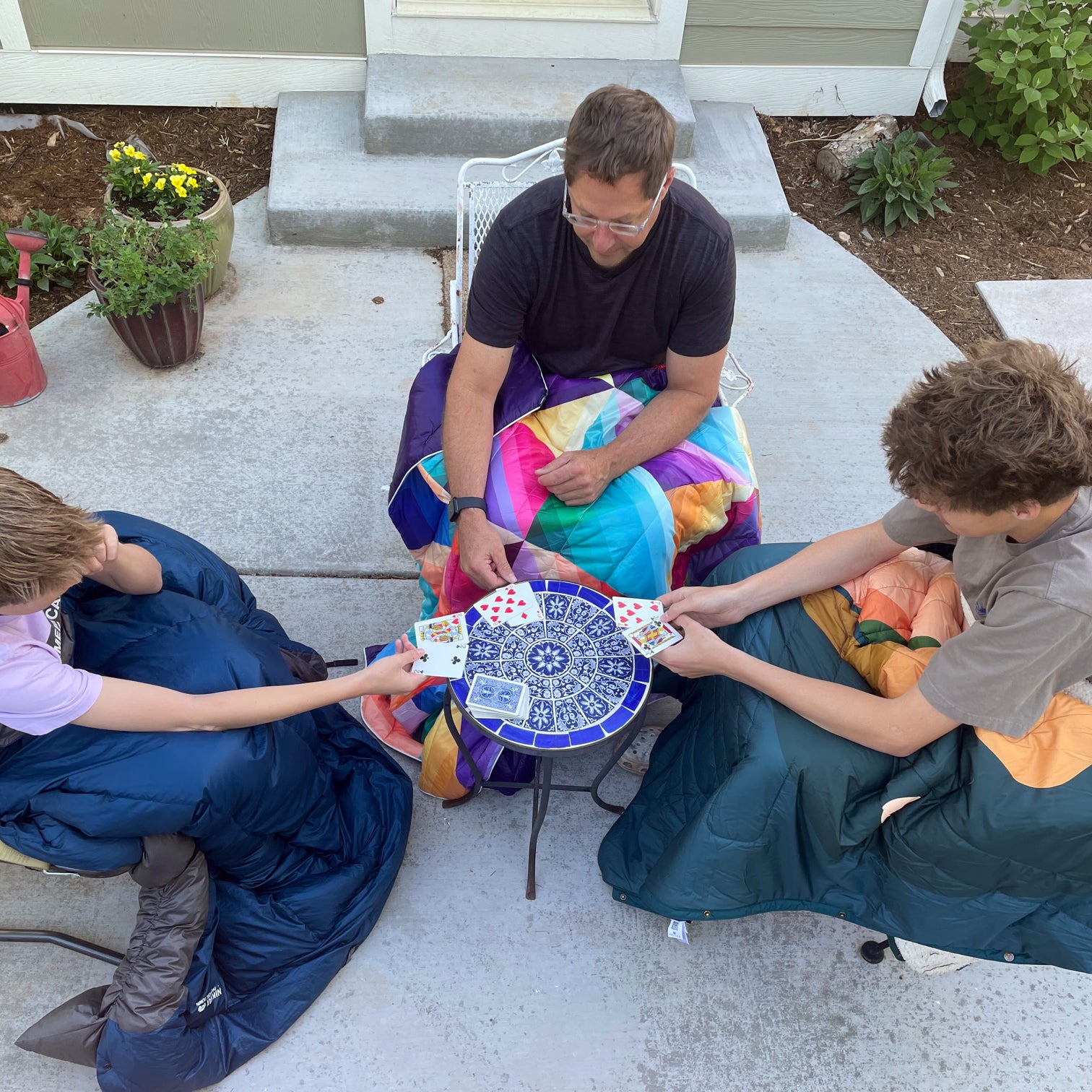 three men playing cards outside with camp blankets around their legs